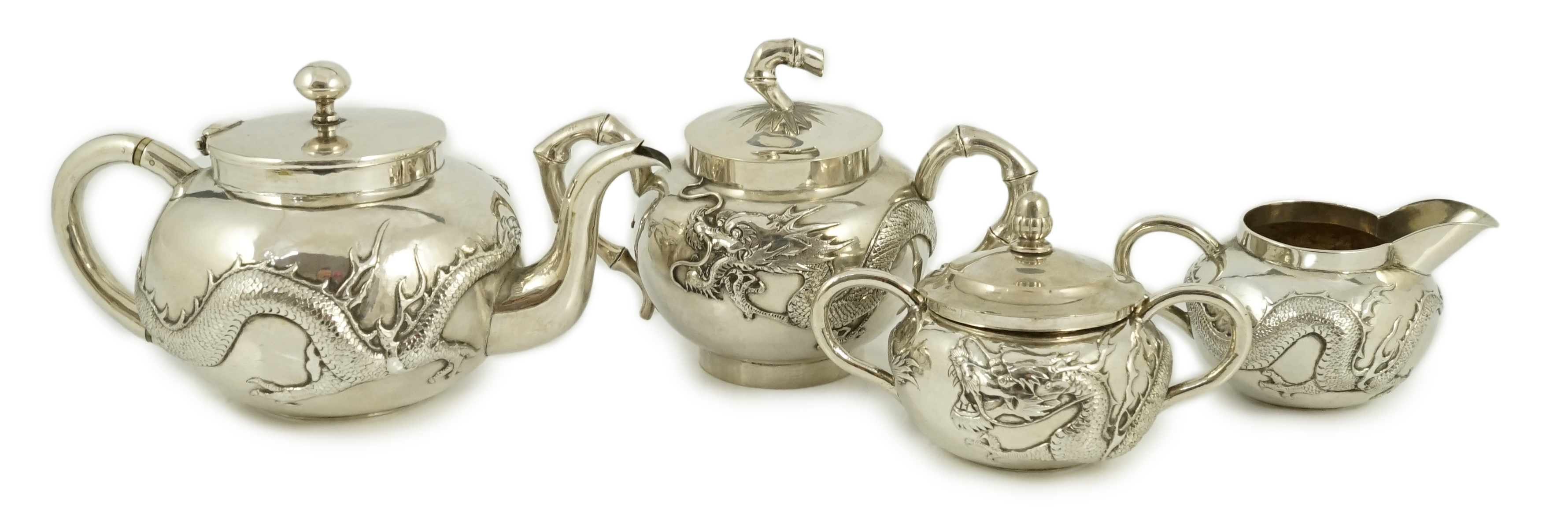 A Chinese three piece silver bachelor's tea set, by TC, decorated with dragon and one other similar Chinese silver two handled sugar bowl and cover, maker Sing Fat? and an odd cover